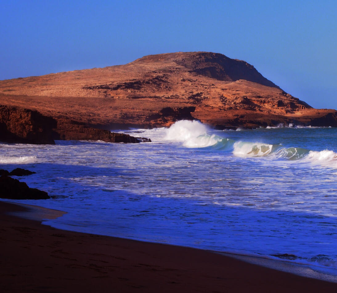 Panoramic view of Cabo de la Vela showing golden desert dunes meeting turquoise ocean waters under blue sky