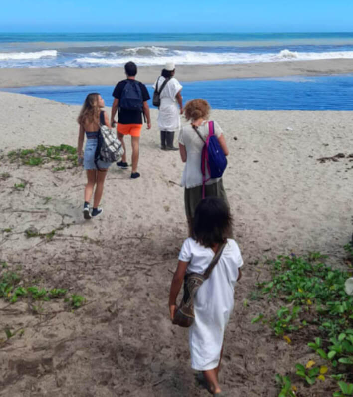 Tourists walking along beach with Arhuaca indigenous child during Katanzama community tour, Caribbean coast of Colombia