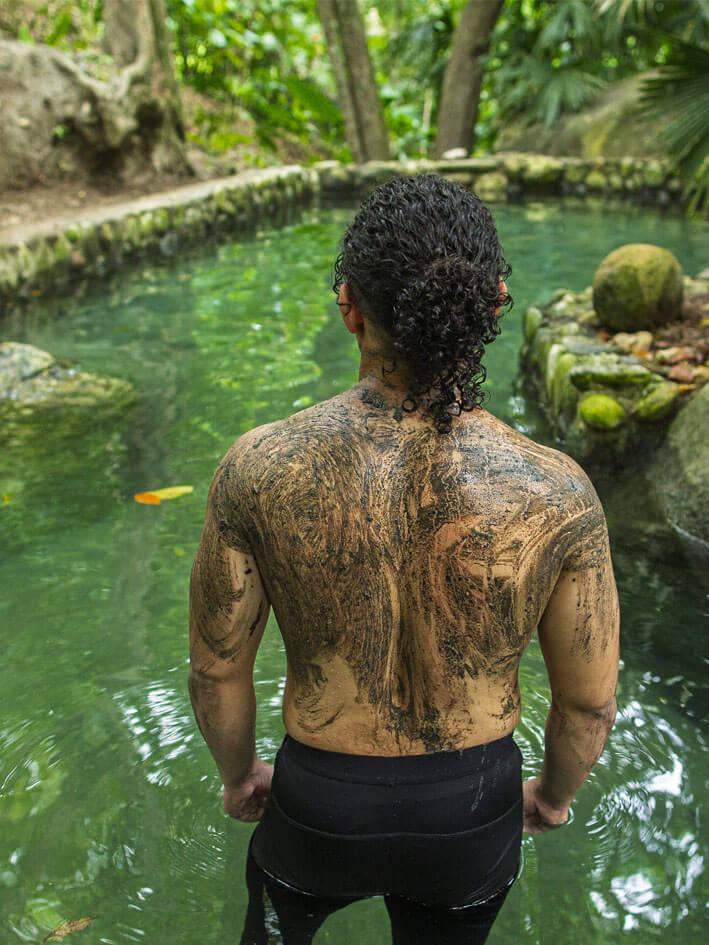 Visitor with ash-painted back contemplating emerald-colored thermal waters after spiritual ceremony at Bunkuany
